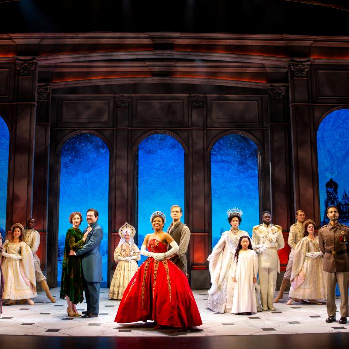 Anastasia in a red ball gown with prince by her side and cast behind her