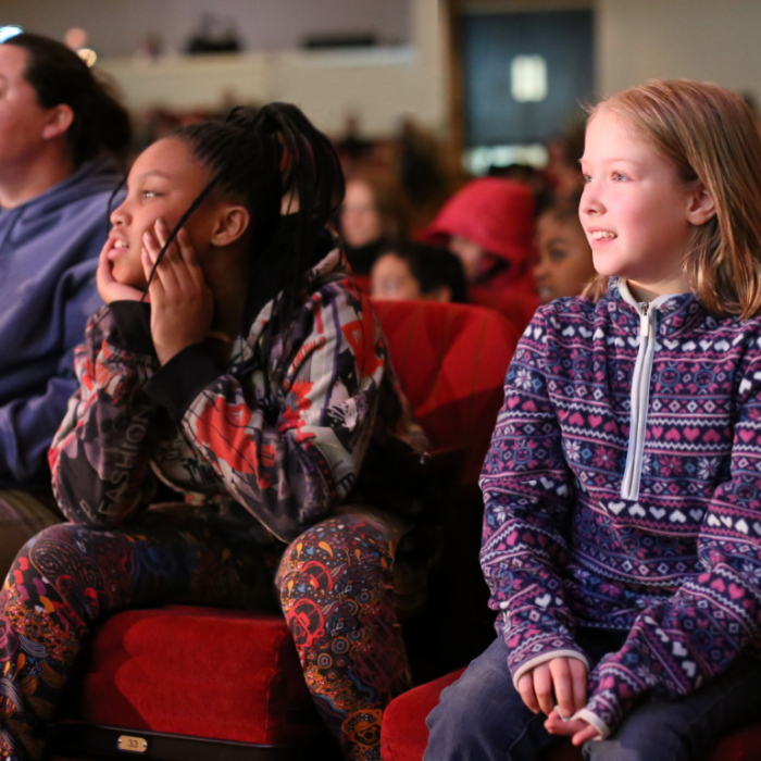 Young girls sitting in the theatre's red chairs listening to a concert
