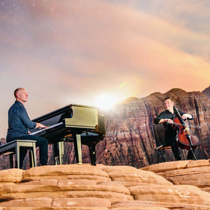 The Piano guys, one on a piano and the other playing a cello on a mountain.