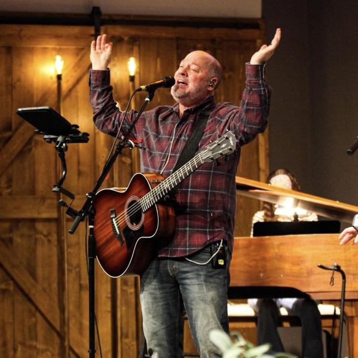 Larry Lowis with a guitar at a mic with hand lifted up