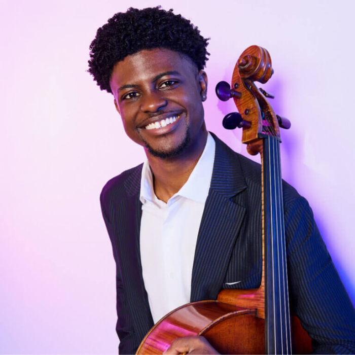 Black musician holding a cello leaning against a wall.