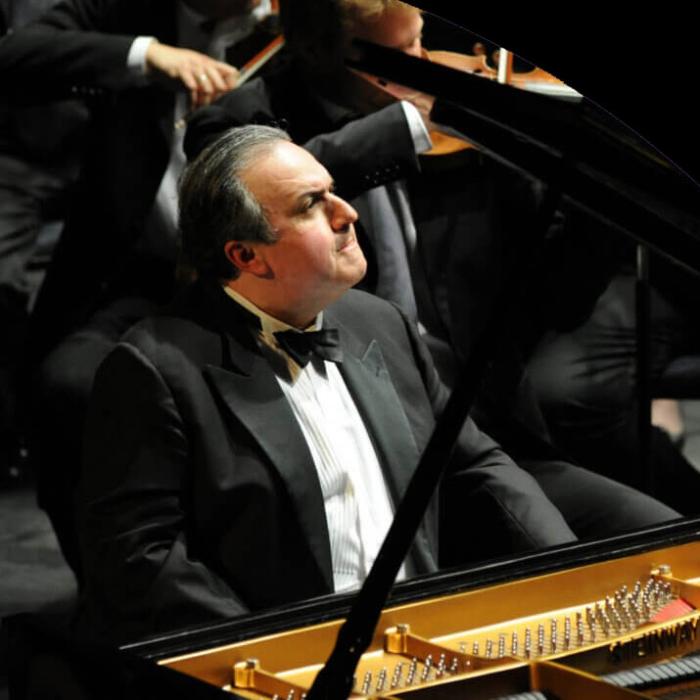 A older man sitting at a grand piano looking at the conductor.
