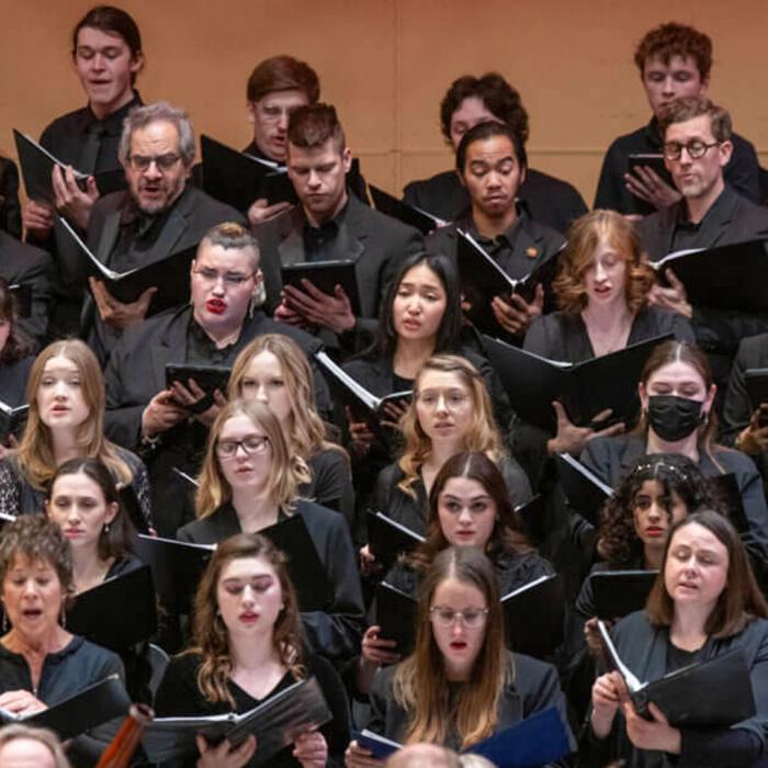 Choir holding black binders of music singing all dressed in black.