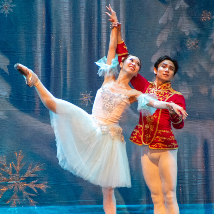 A ballerina with her leg in the air being held by another dancer in a red suit.