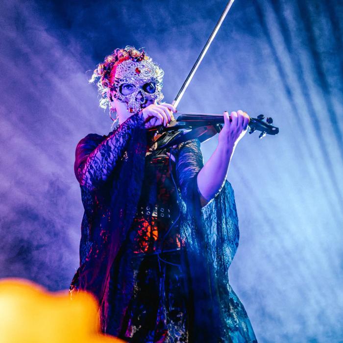 A lady playing the violin with a beautiful jeweled mask on.