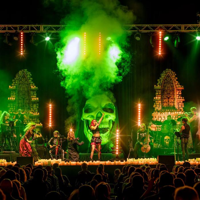 A concert scene with green smoke in front of a skull with singer and band members on the stage