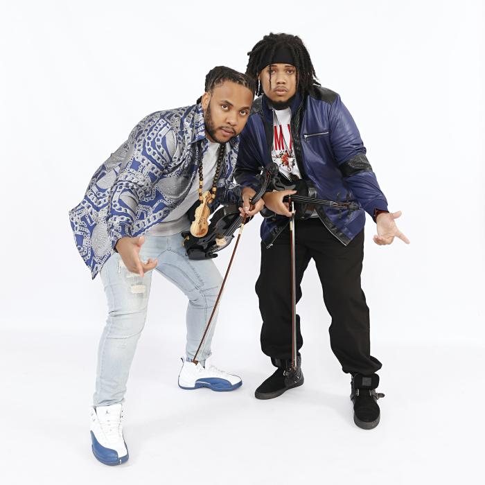 Promotional photo of the Sons of Mystro, two guys holding violins with hands extended.