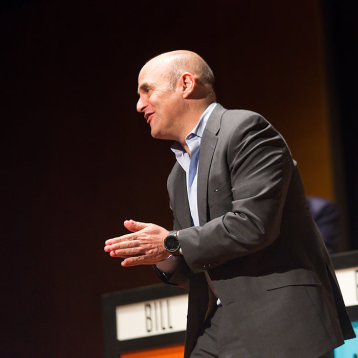 A man in a grey suit on staging clapping 