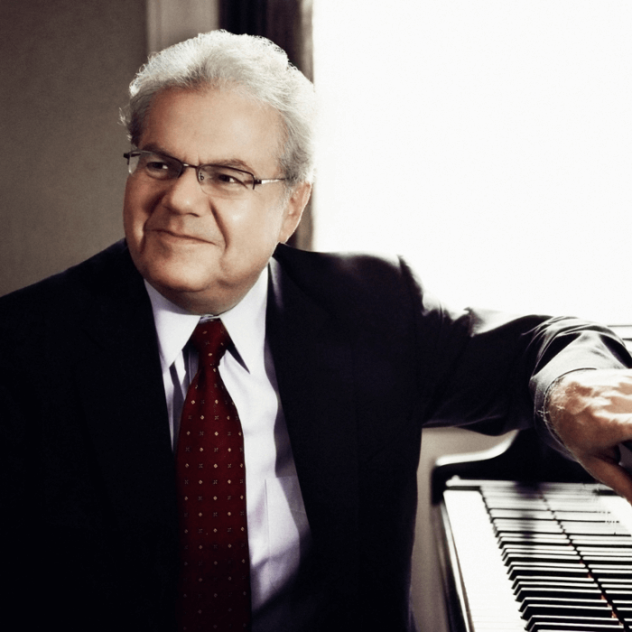 Man sitting at a piano with this elbow resting on the top of the piano.