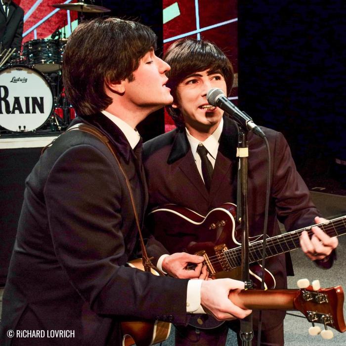 Two Beatle performers singing into a mic.