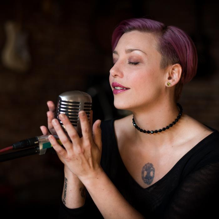 Lady with purple highlights in her hair holding an old fashion mic singing